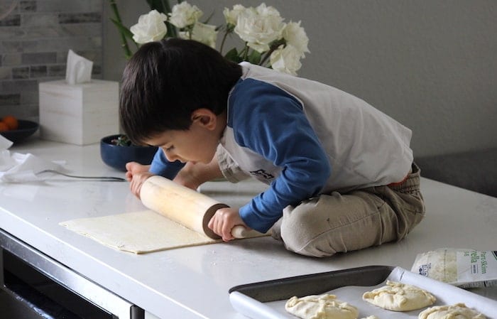 Child rolling out dough for cheese buns