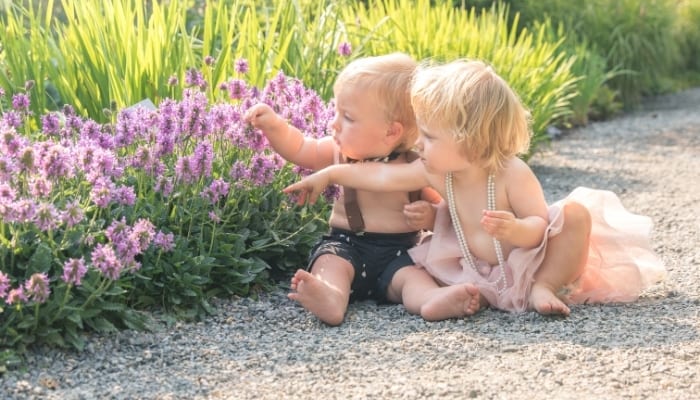 baby boy and girl sitting on the ground playing with flowers