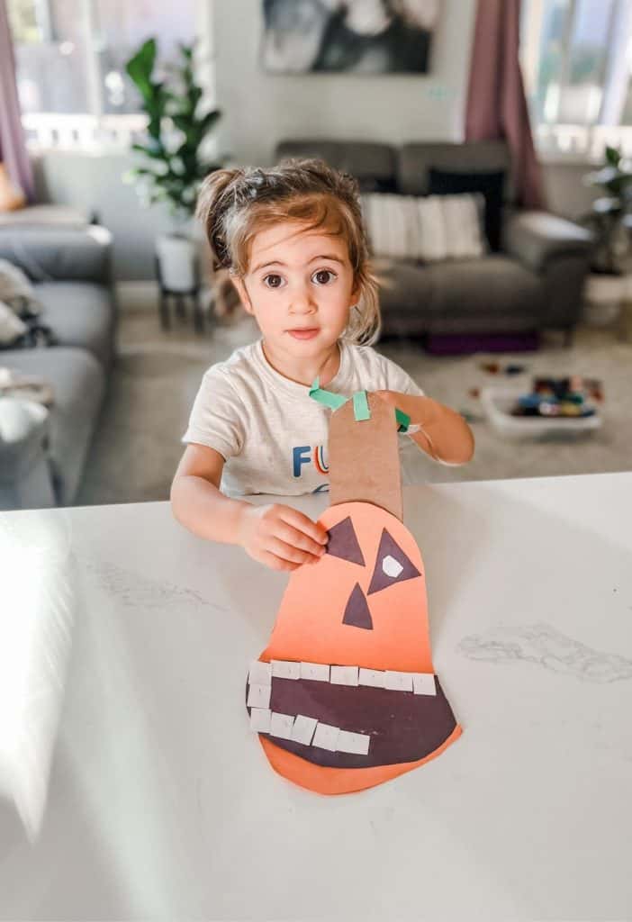 a toddler girl holding a Halloween craft for 2-year-olds