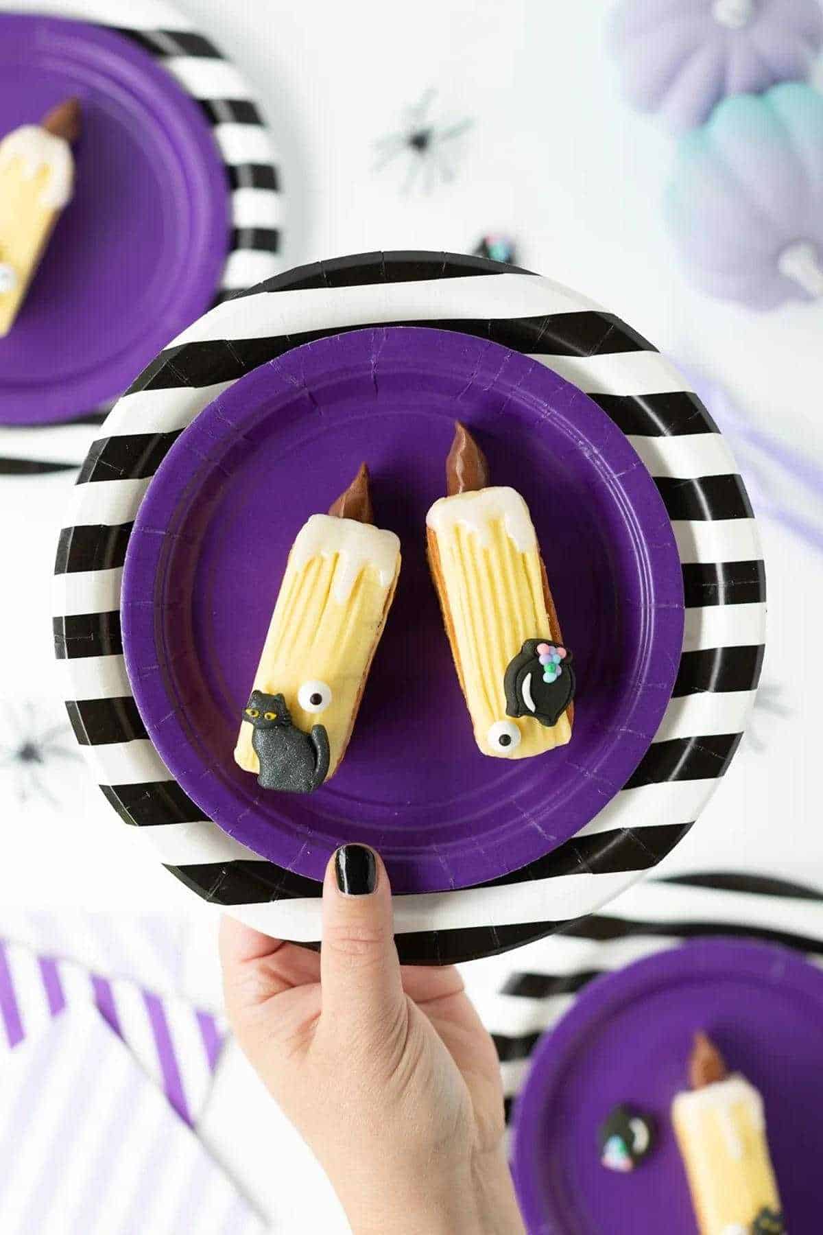 A person is holding a plate two mini candle-themed cakes for hocus pocus-themed party.