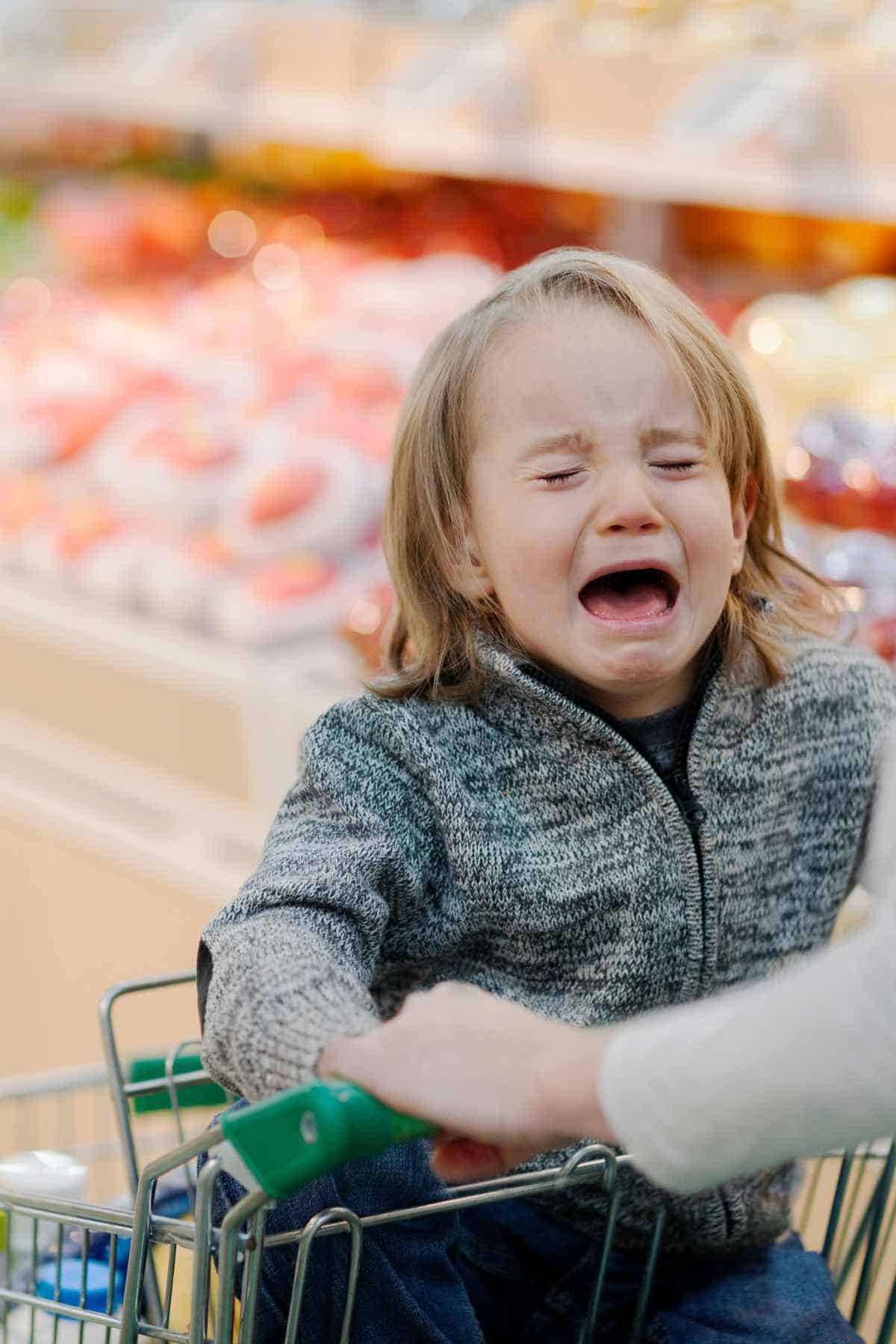 A child crying in a shopping cart in a grocery store when running errands.