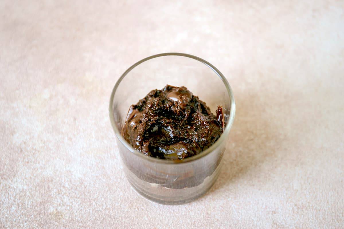A glass pudding cup with crushed cookie powder and chocolate pudding on top of it.