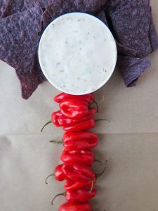 A bowl of dip with purple chips and red peppers as a body and head of the veggie skeleton tray.