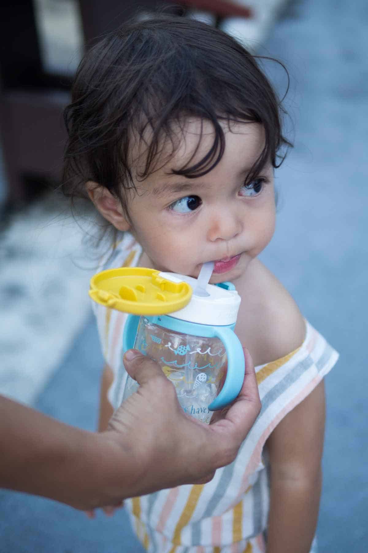 A little girl is drinking from a bottle with a straw.