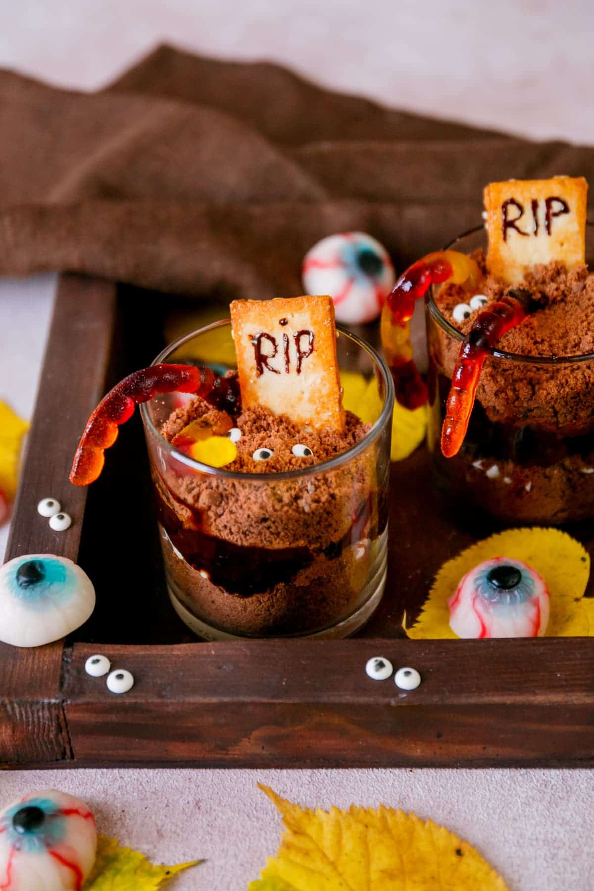 A tray of graveyard dirt cups on a wooden table decorated with edible eyeballs.