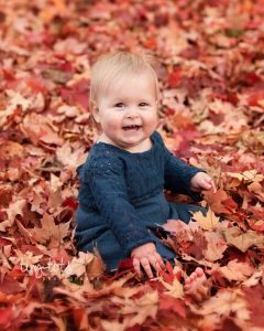 A fall baby photoshoot featuring a baby sitting in a pile of leaves.