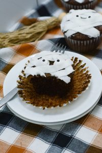 A mummy cupcake displayed with a fork on a white plate.