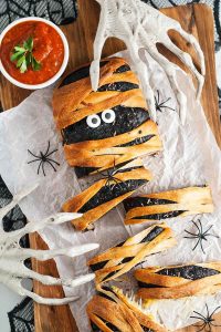 Halloween-themed mummy bread with dipping sauce on a wooden cutting board.