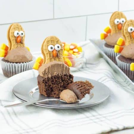 Thanksgiving turkey cupcakes on a table with one on a plate and a piece on a fork.