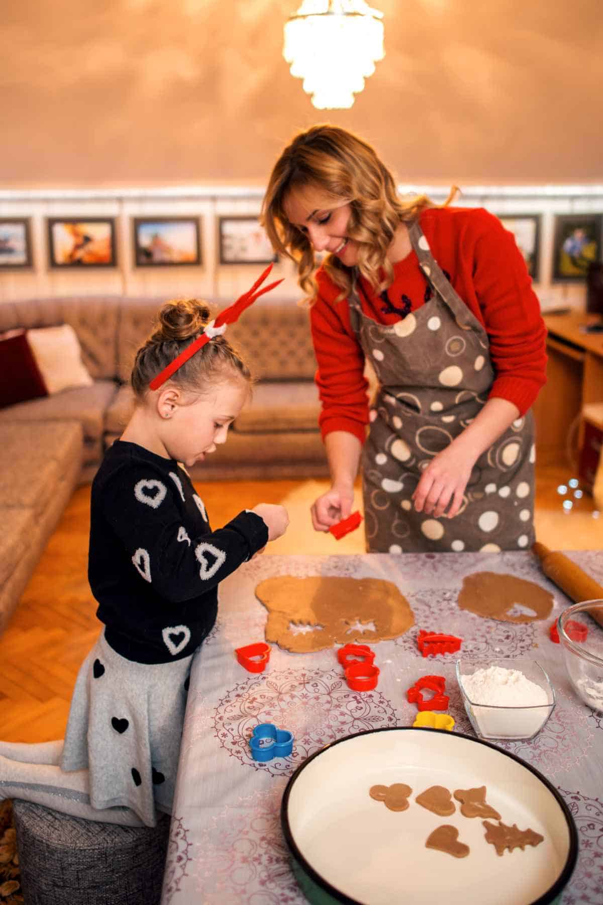 A mother and daughter engaging in a fun Christmas activity for kids, making gingerbread cookies in a cozy living room.