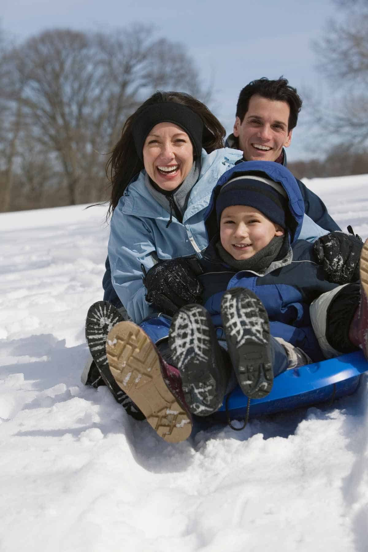 A family is enjoying Christmas activities as they sled down a snowy hill.