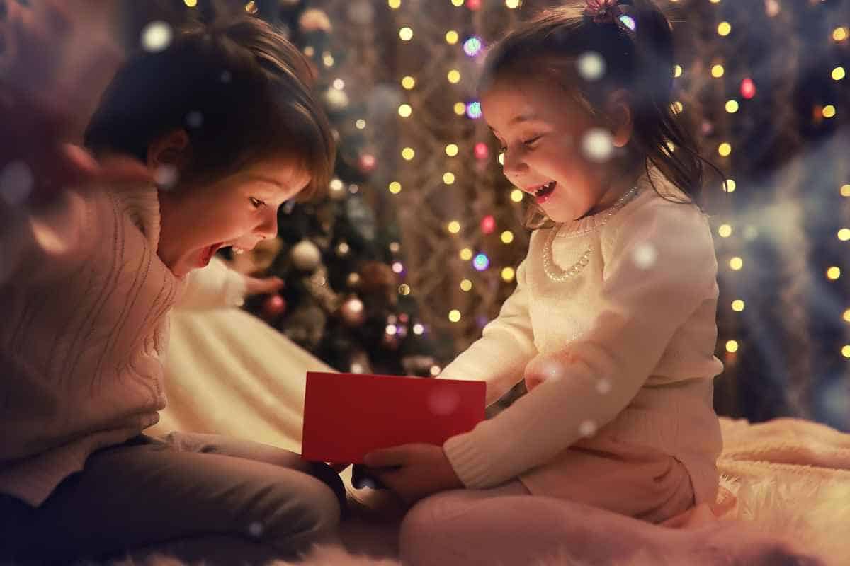 Two children opening a Christmas eve box in front of a Christmas tree.