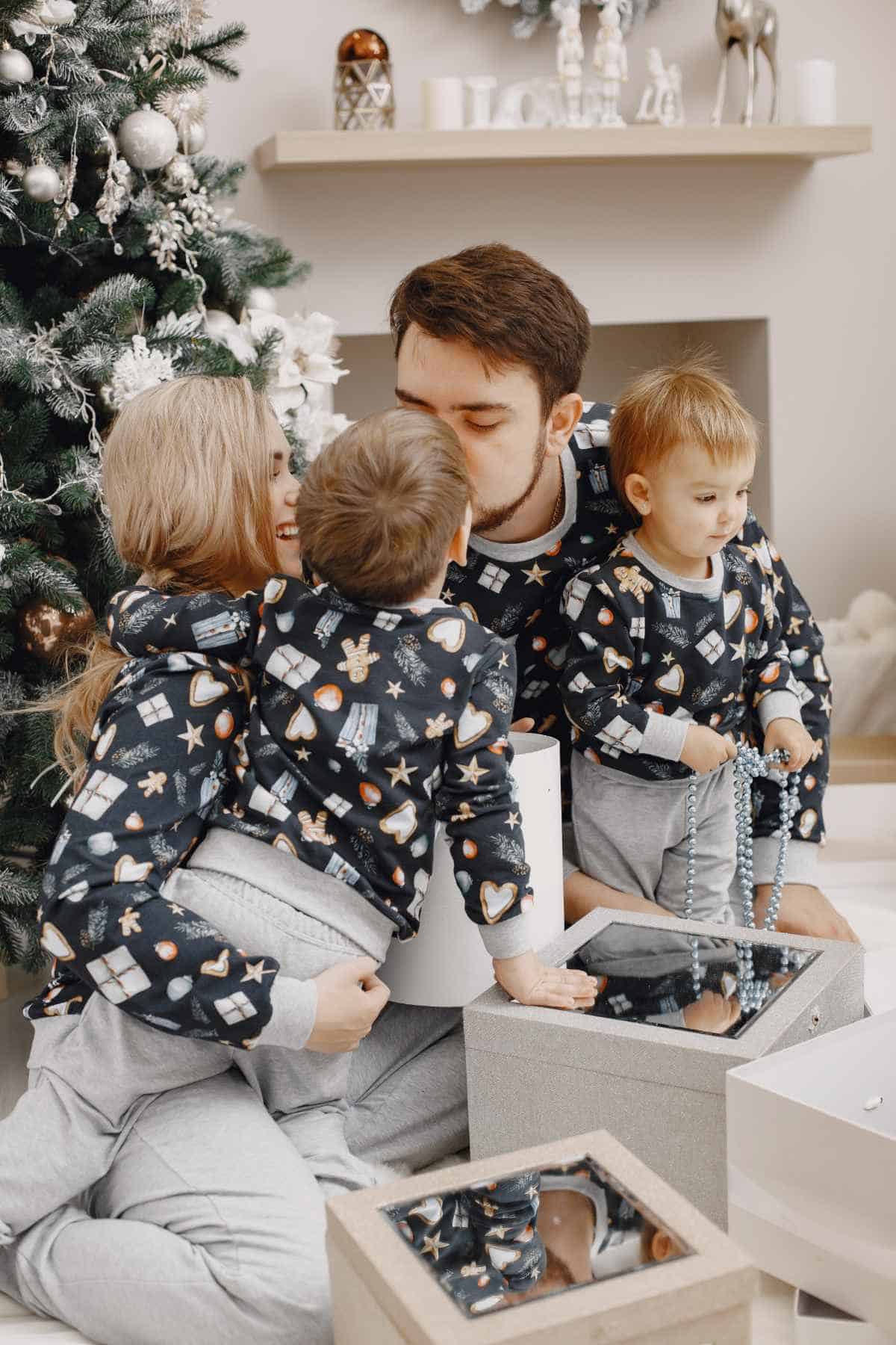 A family is sitting on the floor in front of a christmas tree in matching family pajamas.