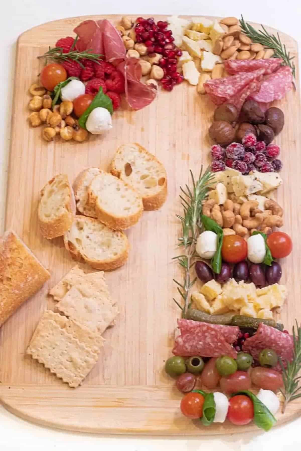 A wooden board with a variety of meats, fruits, bread, and cheeses on it.