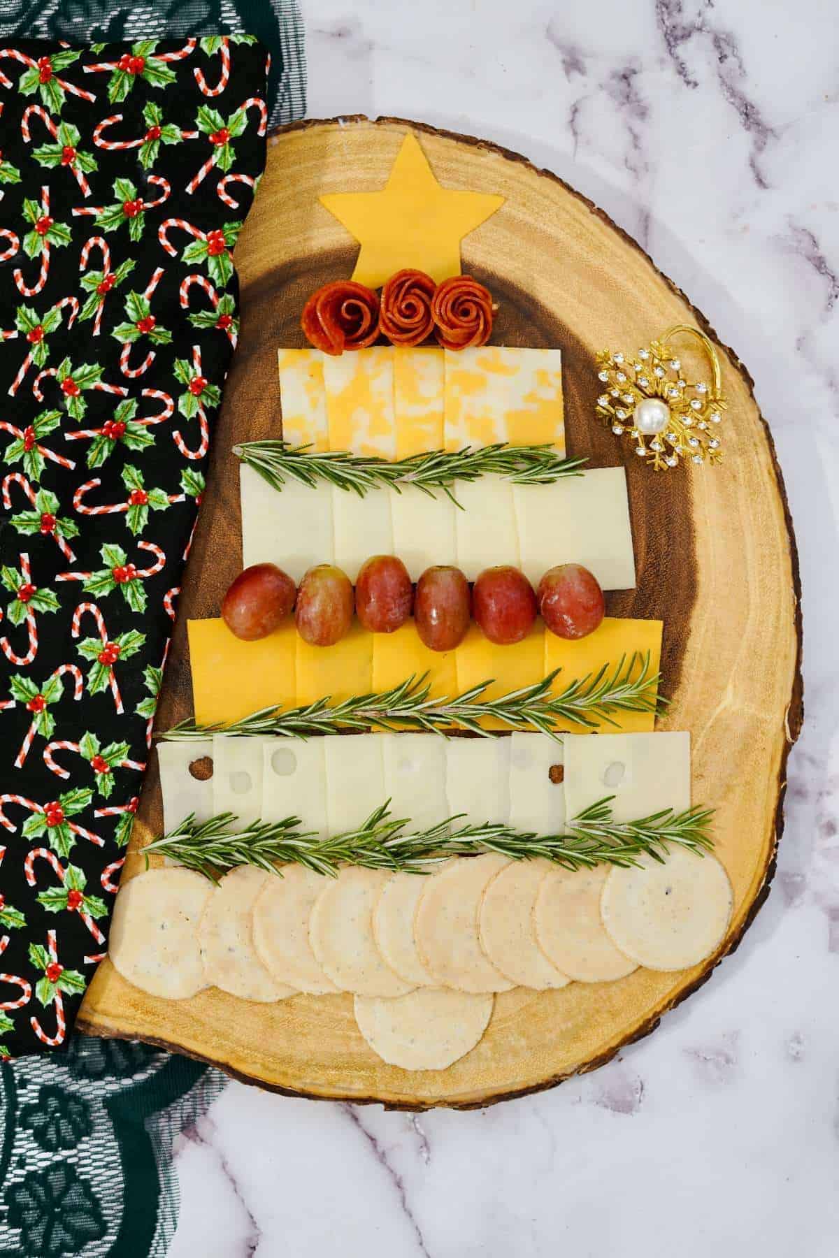 A Christmas tree on a wooden board made of cheese, meat, and grapes.