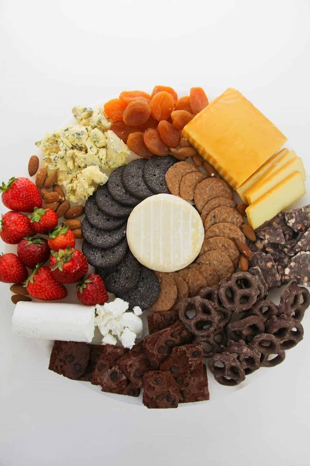 A platter with a variety of cheeses, fruits, and crackers.