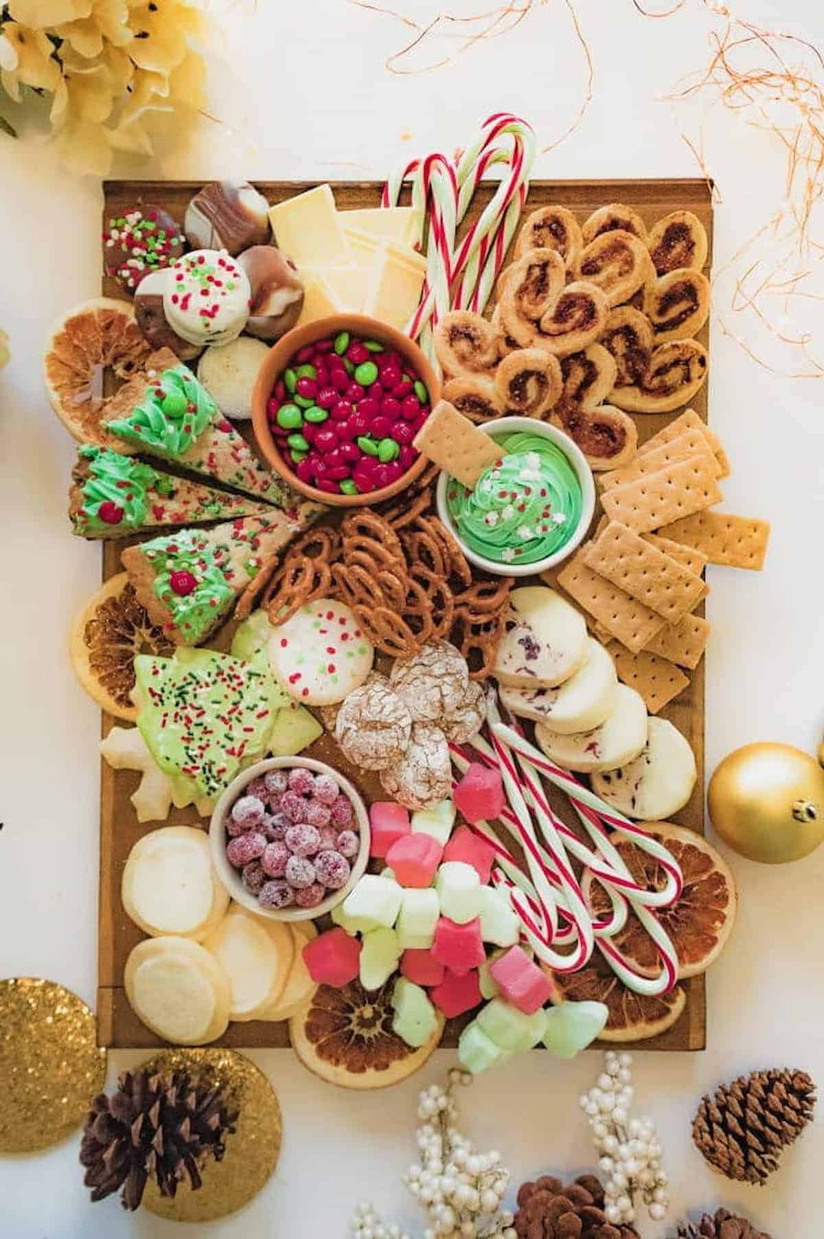 A tray of Christmas cookies, cheese, crackers, and candies on a table.