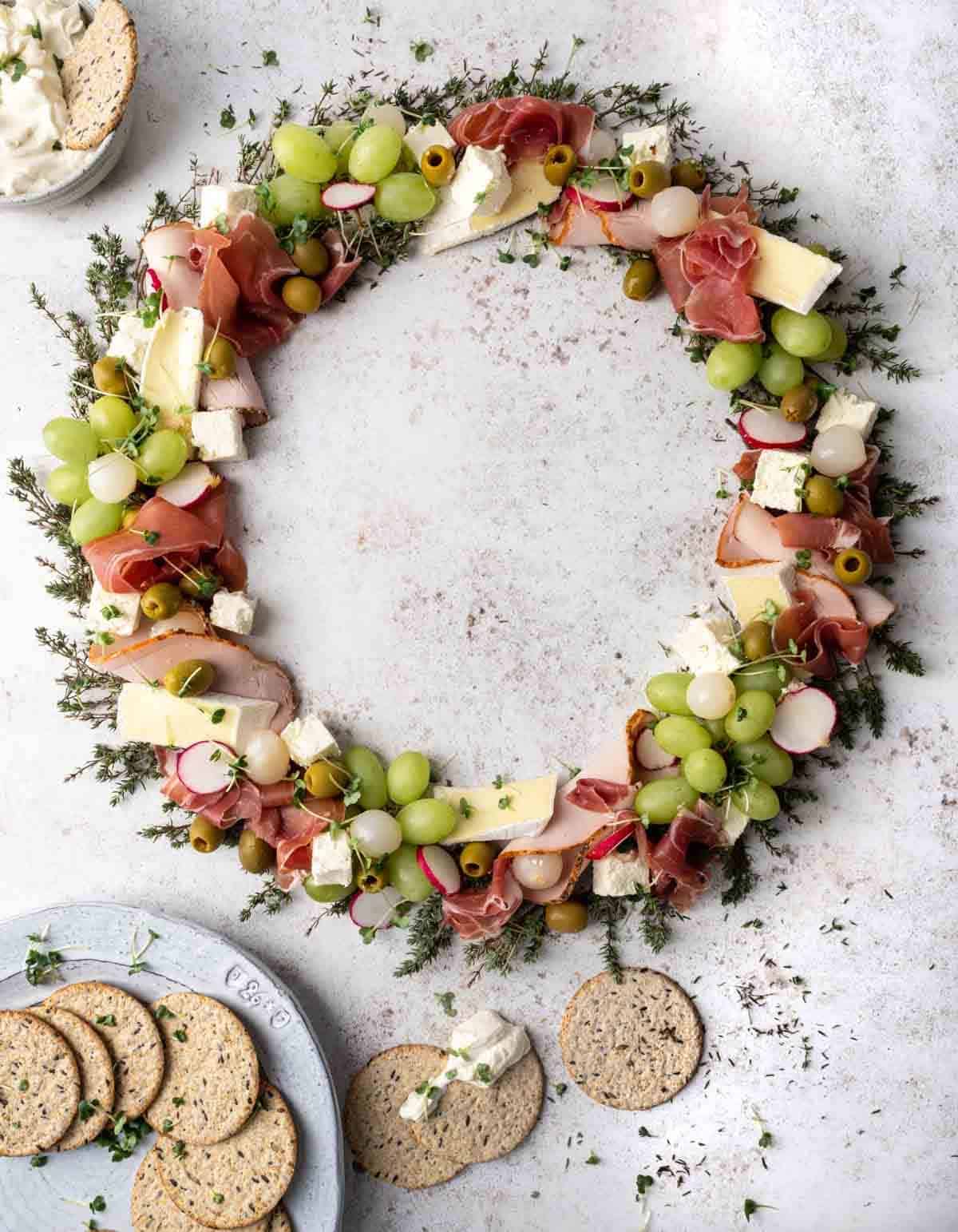 A Christmas charcuterie wreath of grapes, cheese and ham with crackers on the side.