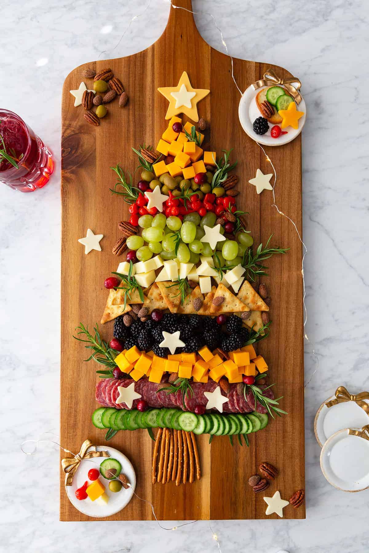 A wooden board with a Christmas tree made of fruits, meat, crackers, and cheese.