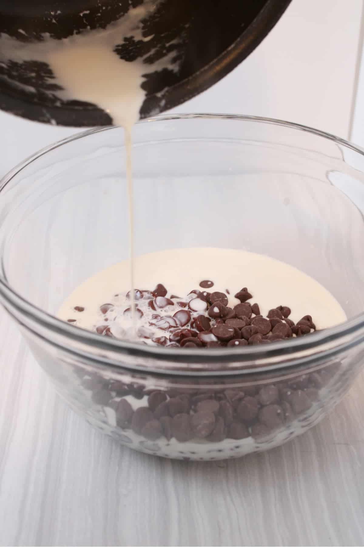 Heated heavy whipping cream being poured into a bowl of chocolate chips .