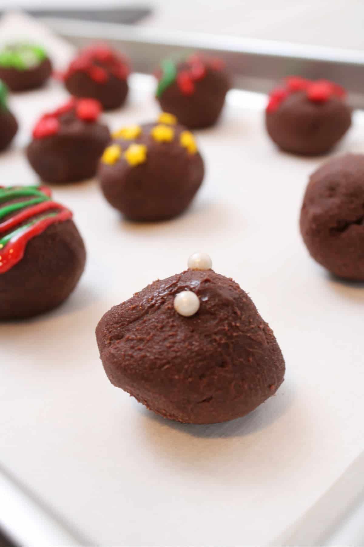 A tray of Christmas truffles with festive sprinkles and icing on them.