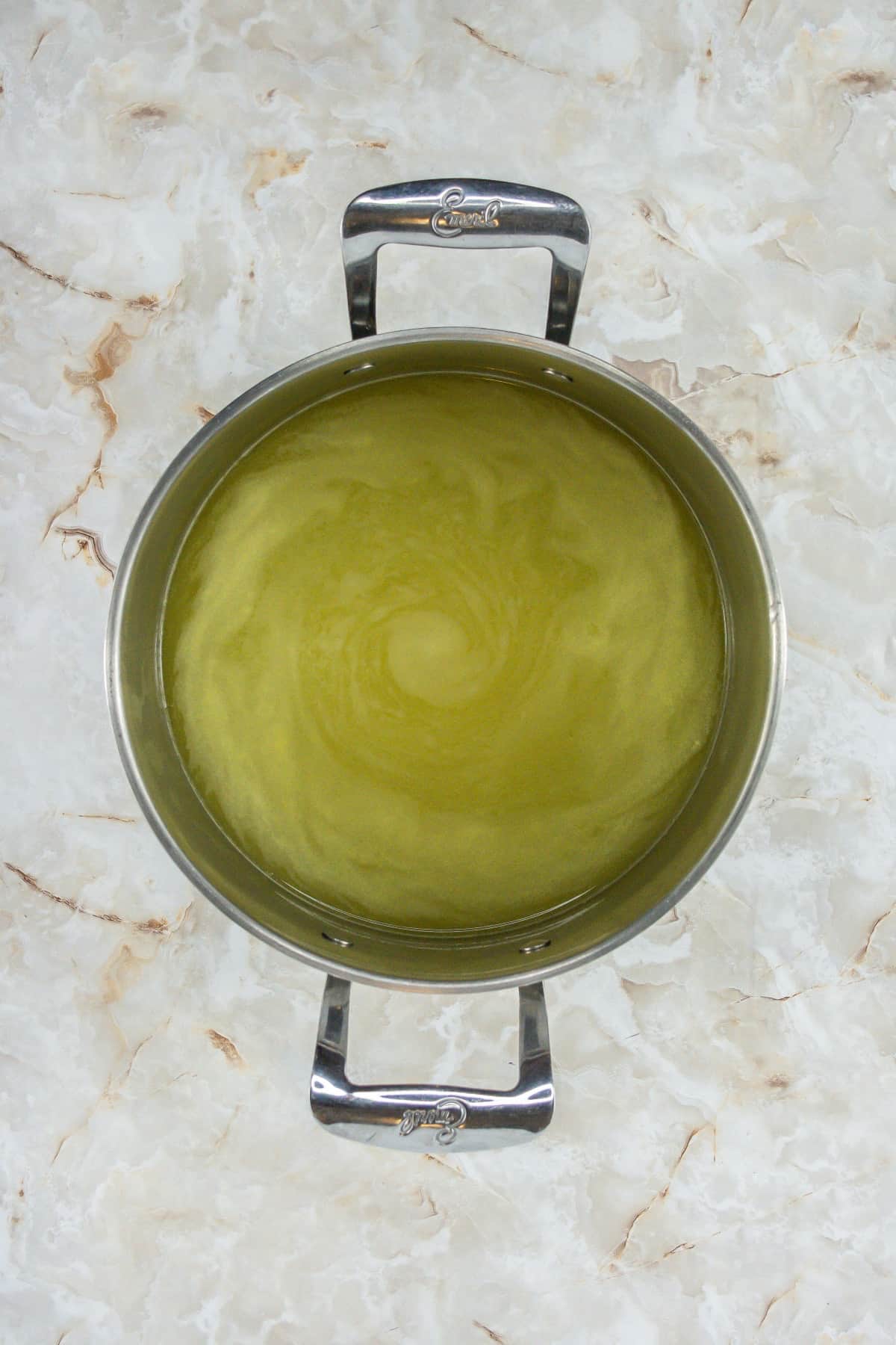 Chicken broth in a pot on a marble surface.