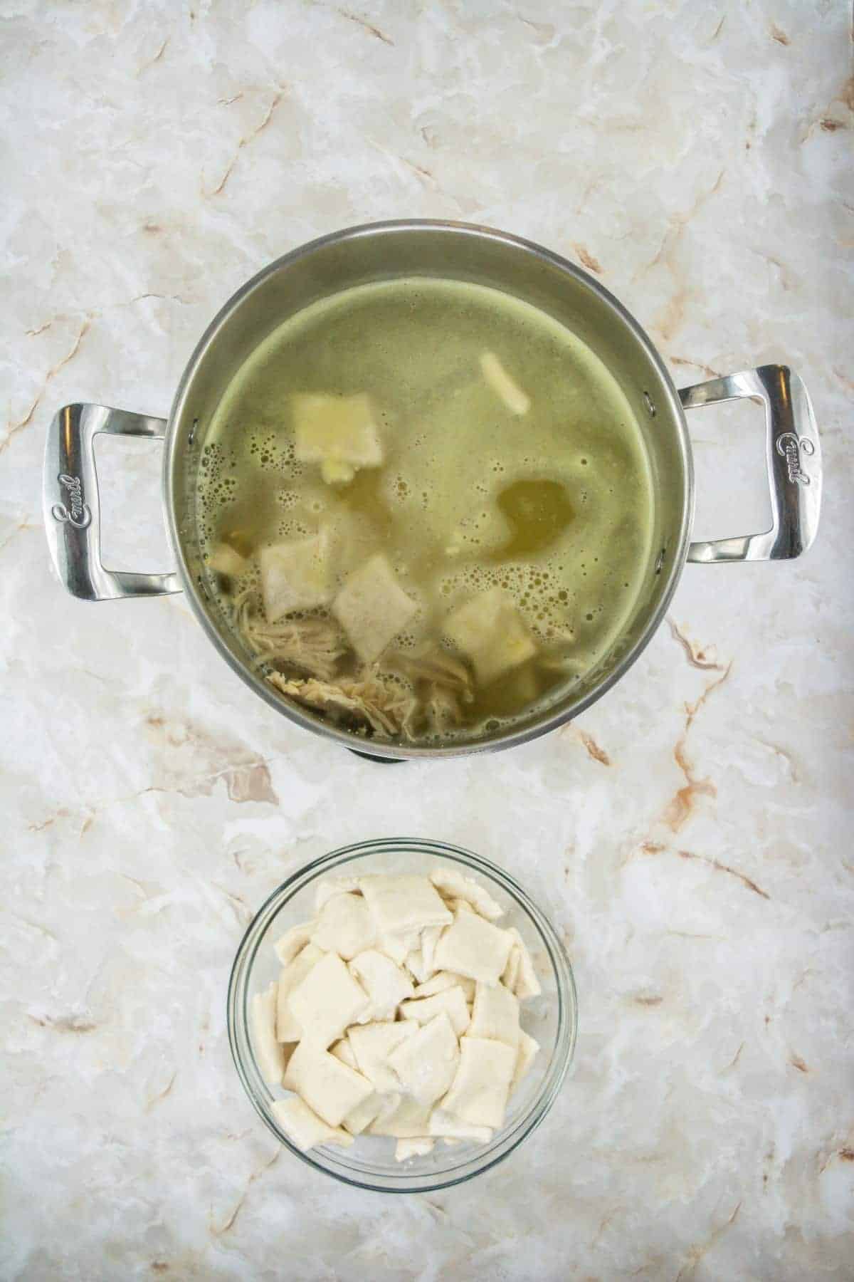 A pot of chicken and dumplings with a bowl of uncooked dumplings next to it.