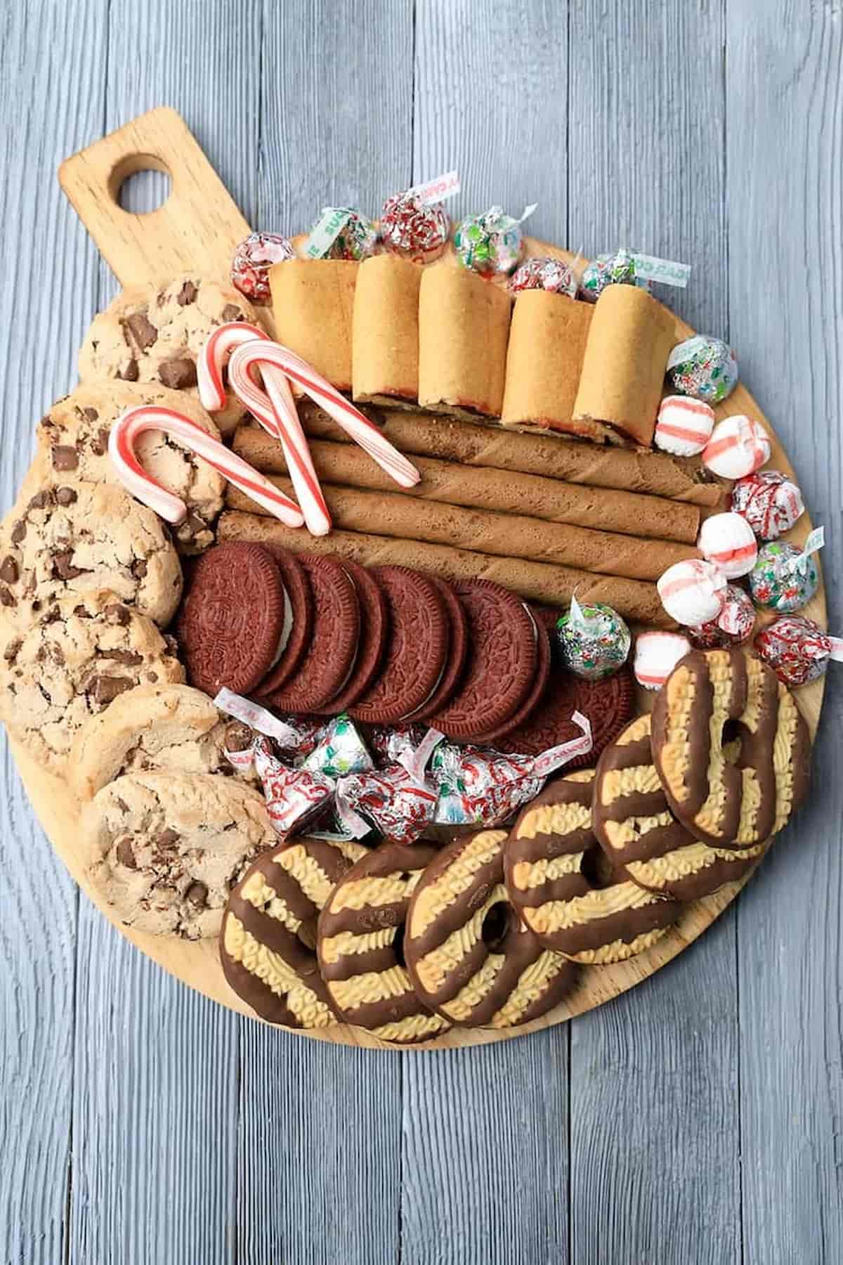 A wooden platter with cookies and candies on it.