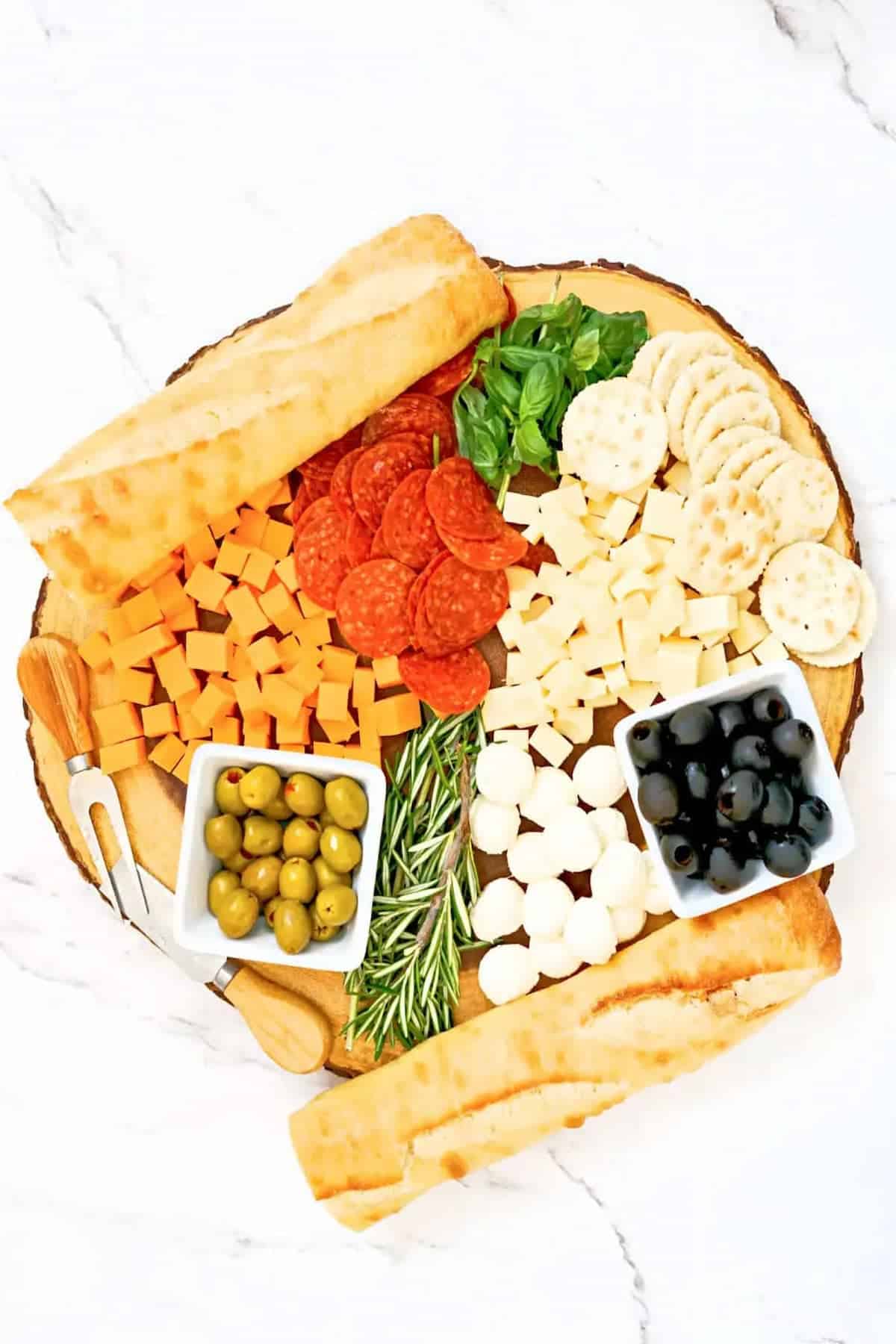 A platter of cheese, olives and crackers on wooden board.