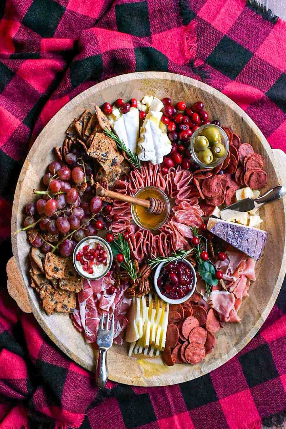 A platter of meats, fruits, and cheeses on a plaid blanket.