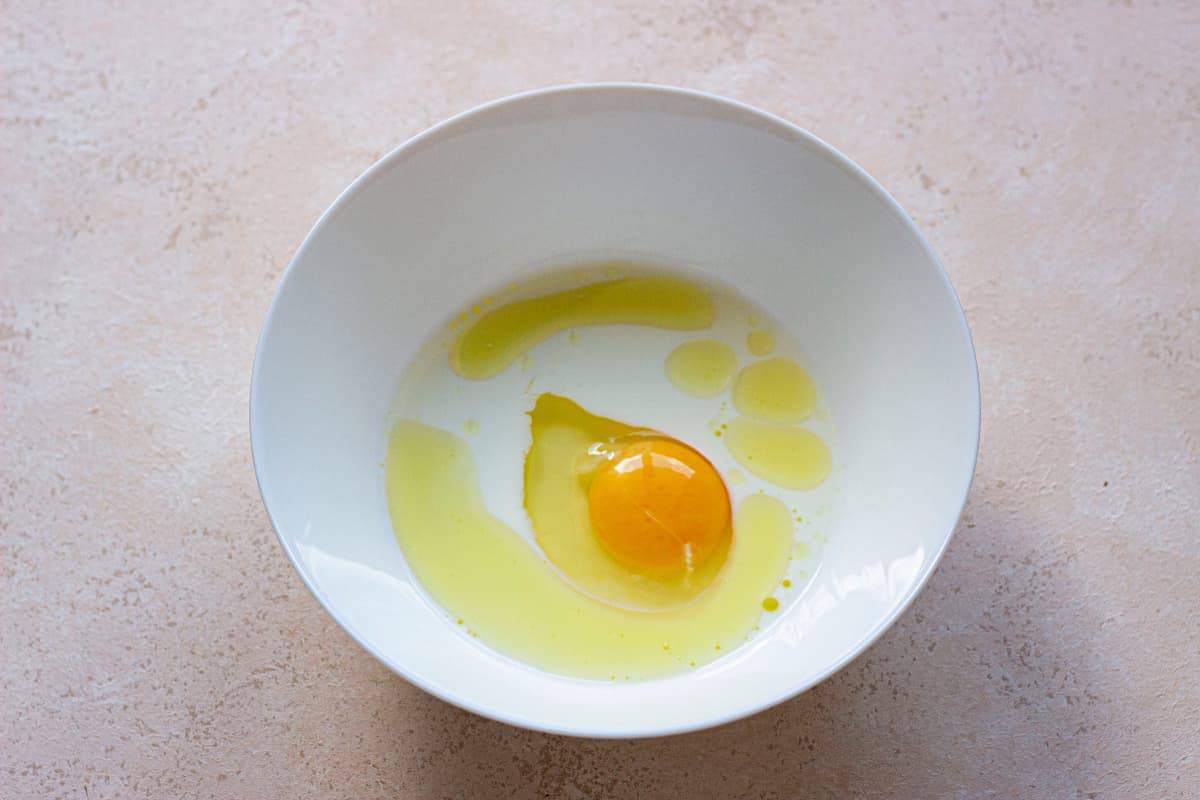 A white bowl with an egg in it.