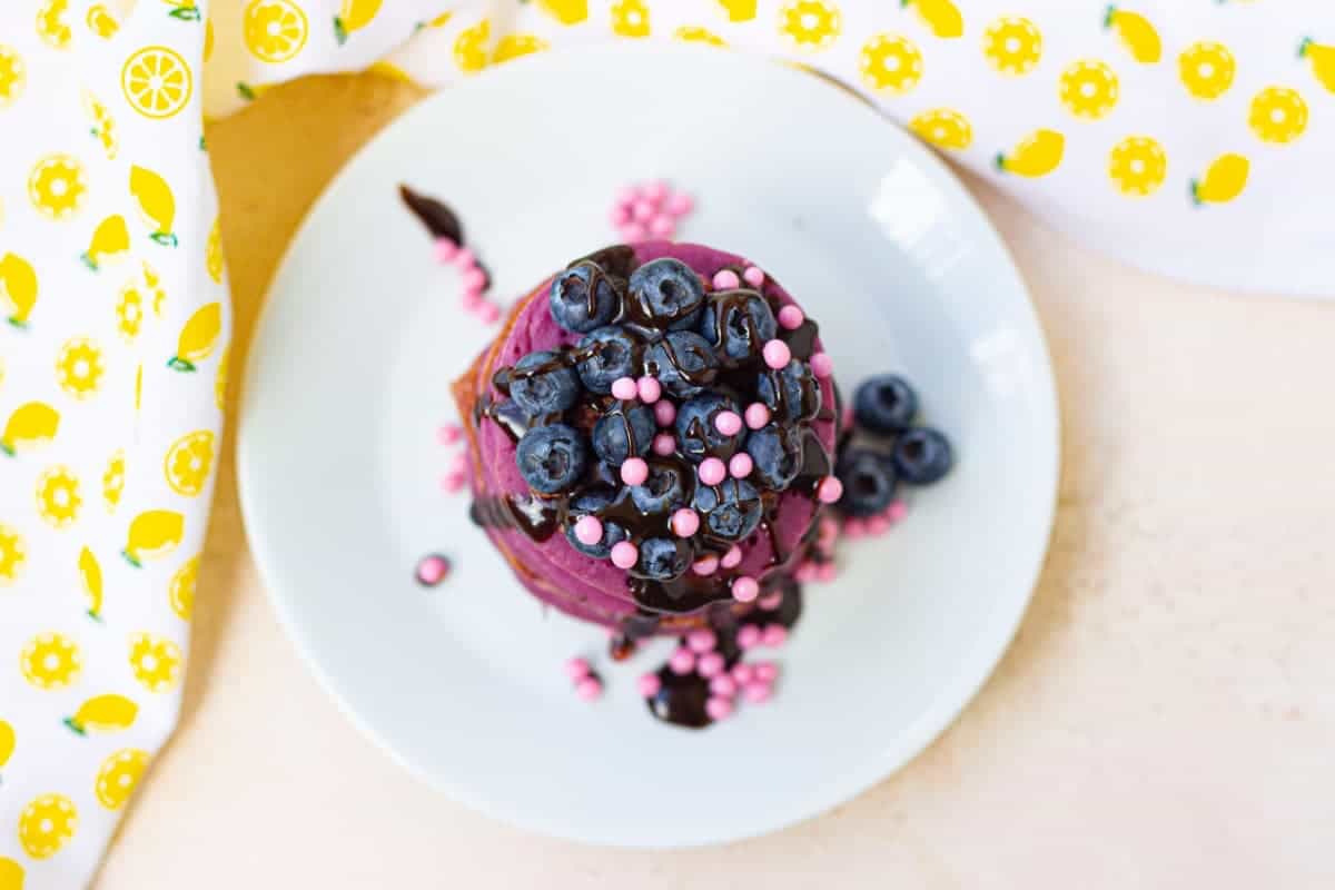A plate of purple pancakes with sprinkles on top.