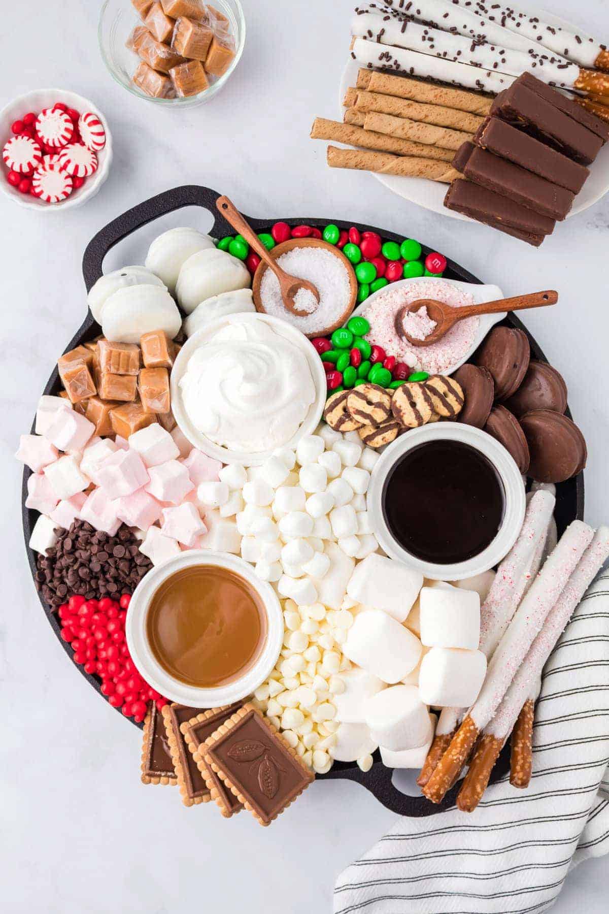 A platter with marshmallows, candies, pretzels, and chocolate dips.