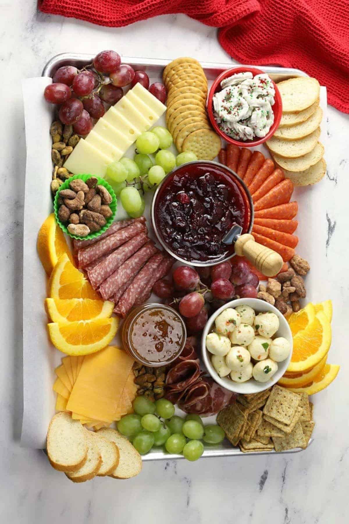 A tray with a variety of cheeses, ,meats, fruits, and crackers on it.