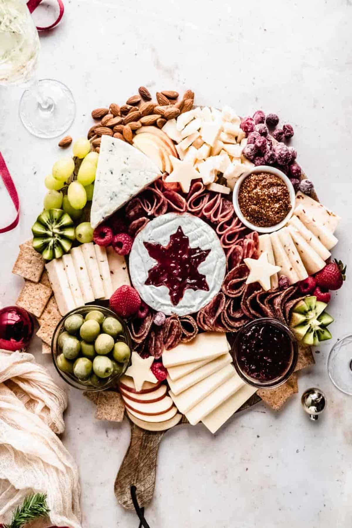 A Christmas tree charcuterie board made out of meat and variety of fruits, cheeses, and nuts.