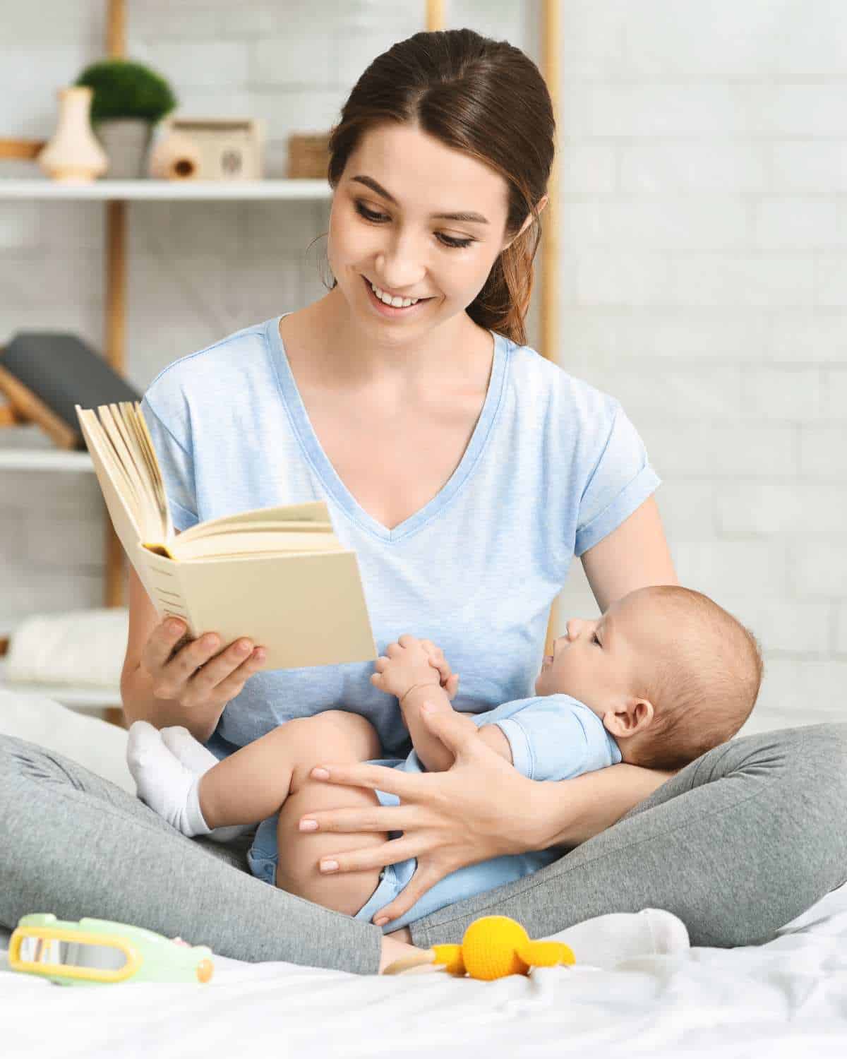 A woman reading a book to her baby on the bed.