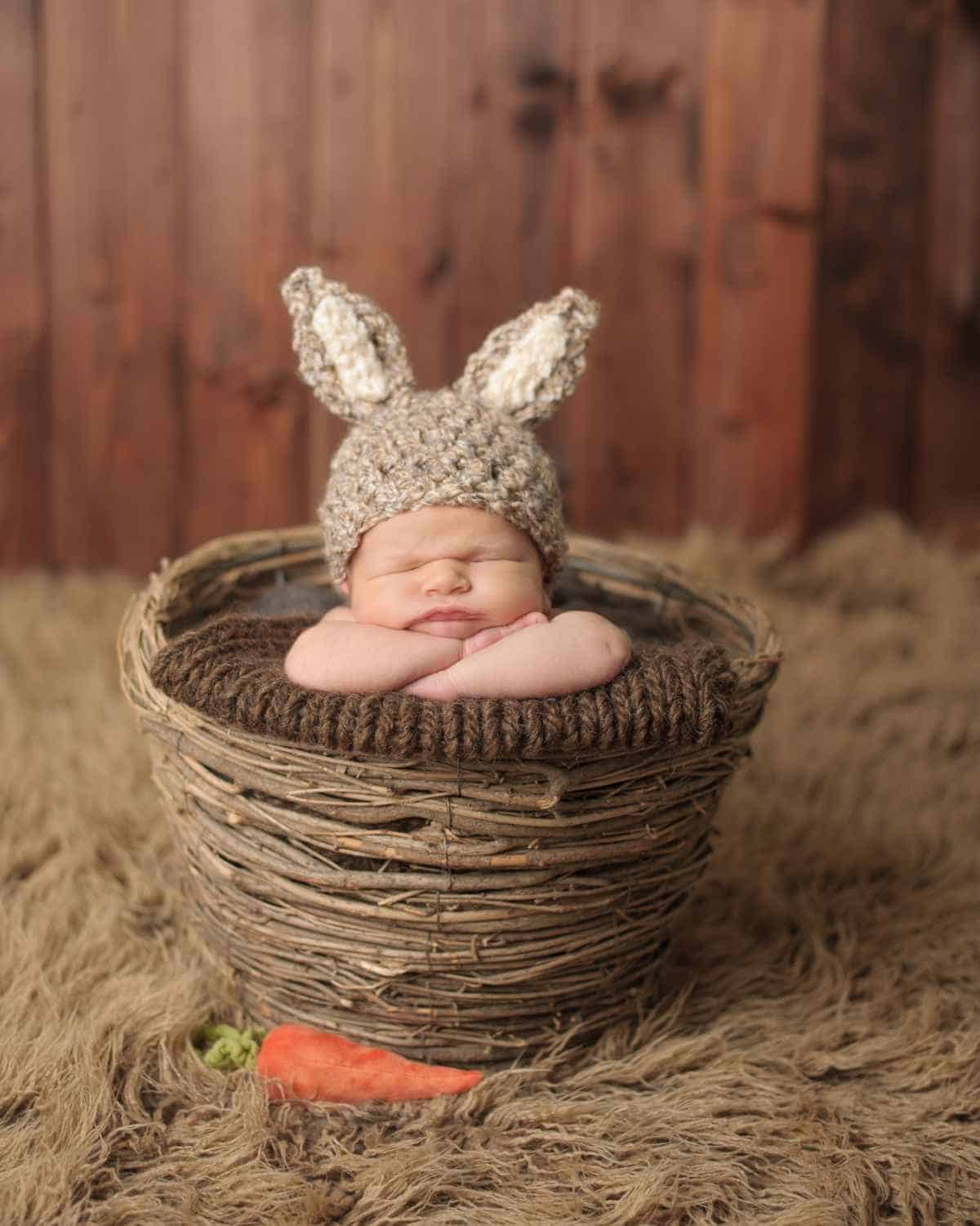 A baby sleeping in a basket wearing a bunny hat.