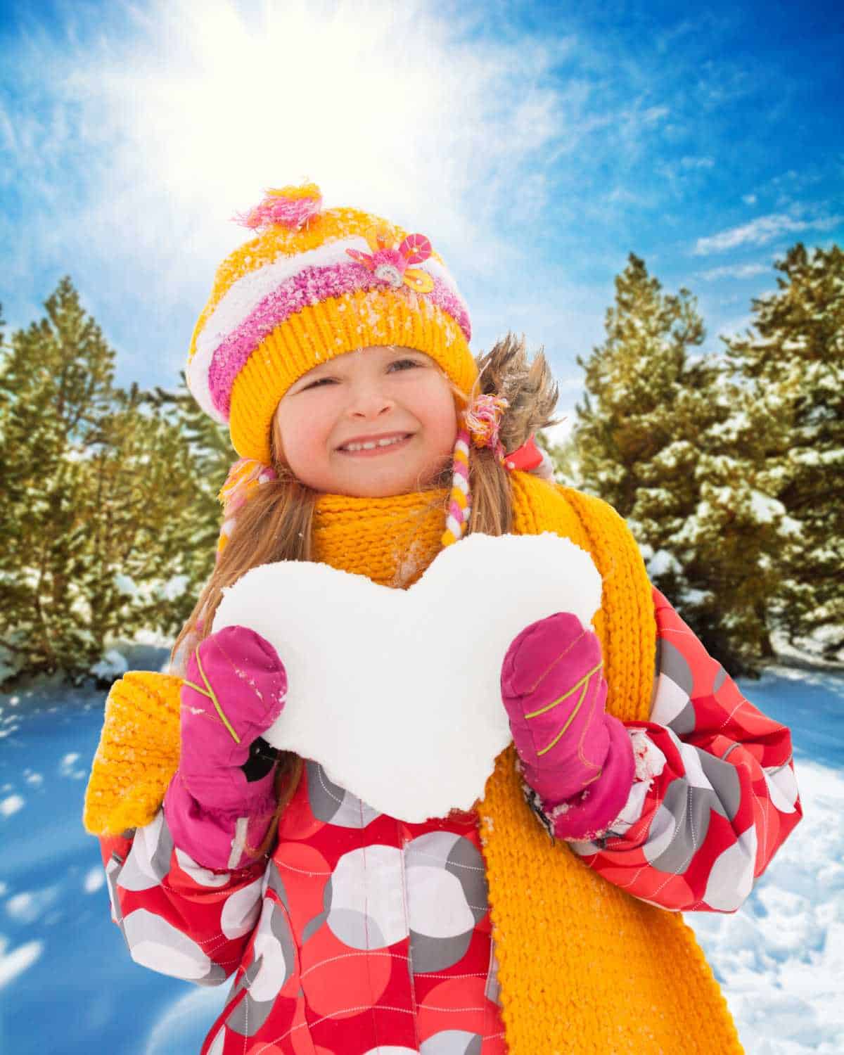 A girl holding a heart shaped snowball.
