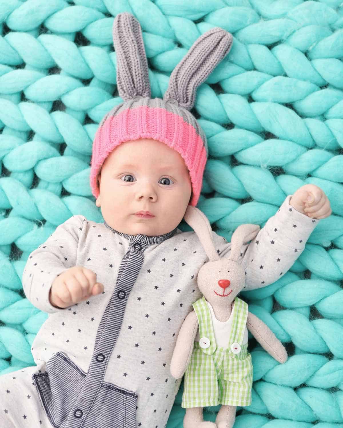 A baby wearing a bunny hat laying on a blue blanket.