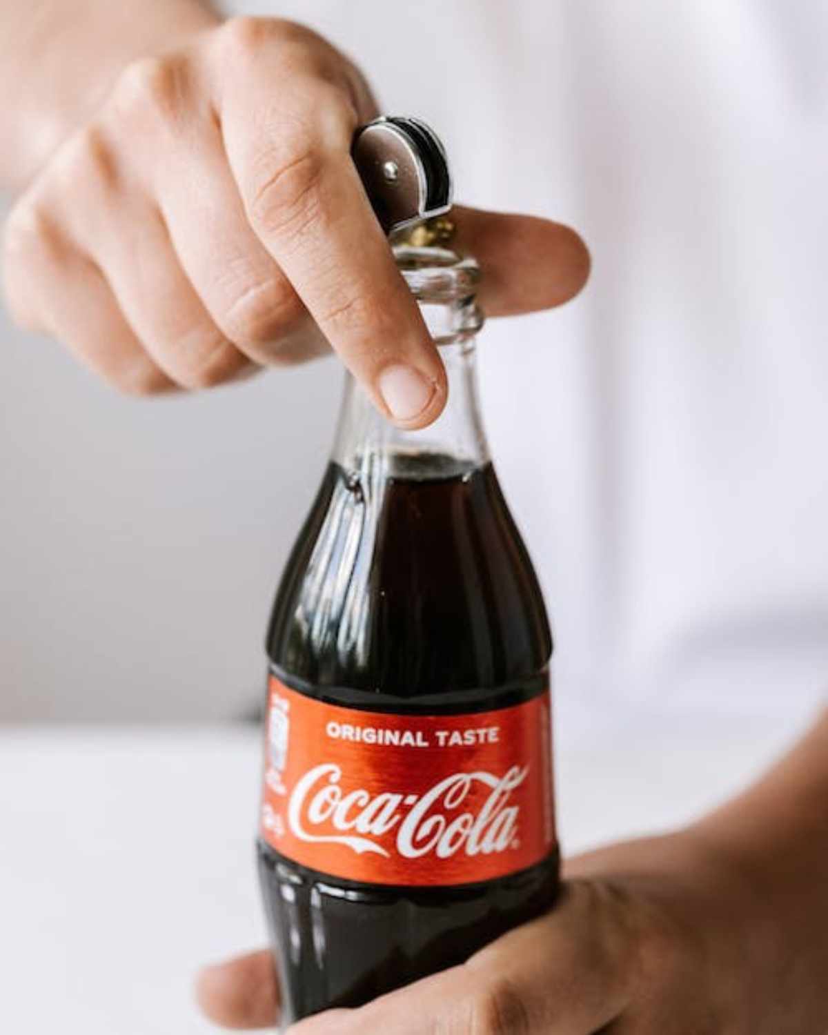 A hand opening a coca cola bottle.