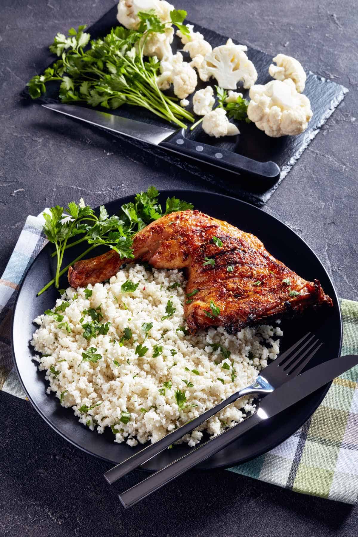 Grilled chicken with cauliflower rice on a black plate.