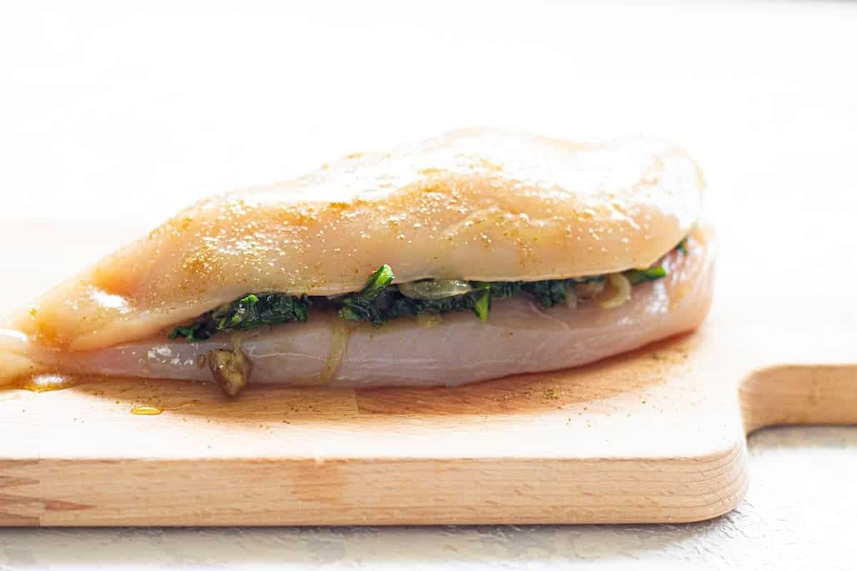 A chicken breast stuffed with spinach is sitting on a cutting board.