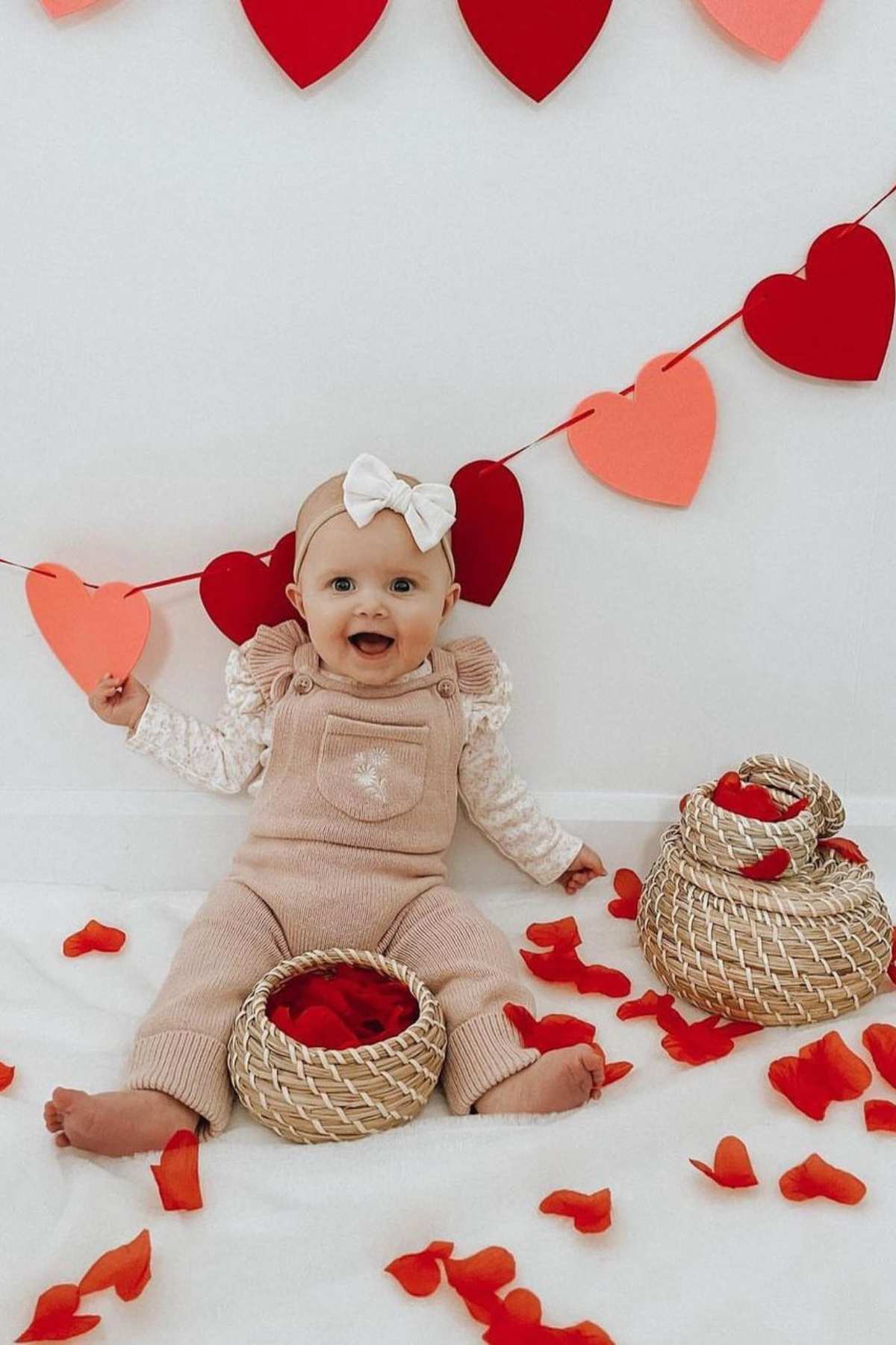 A baby sitting on the floor with hearts and baskets.