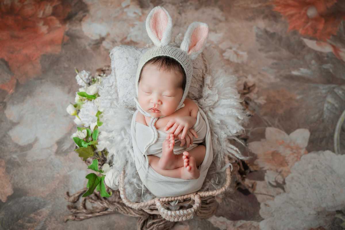 A newborn baby wearing a bunny hat is laying in a basket.