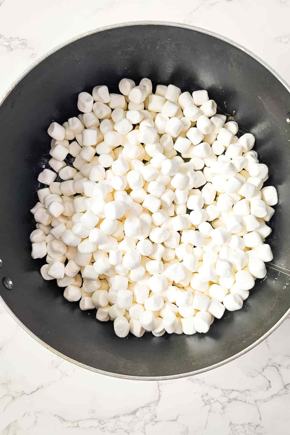 A black pan filled with white marshmallows on a marble surface.