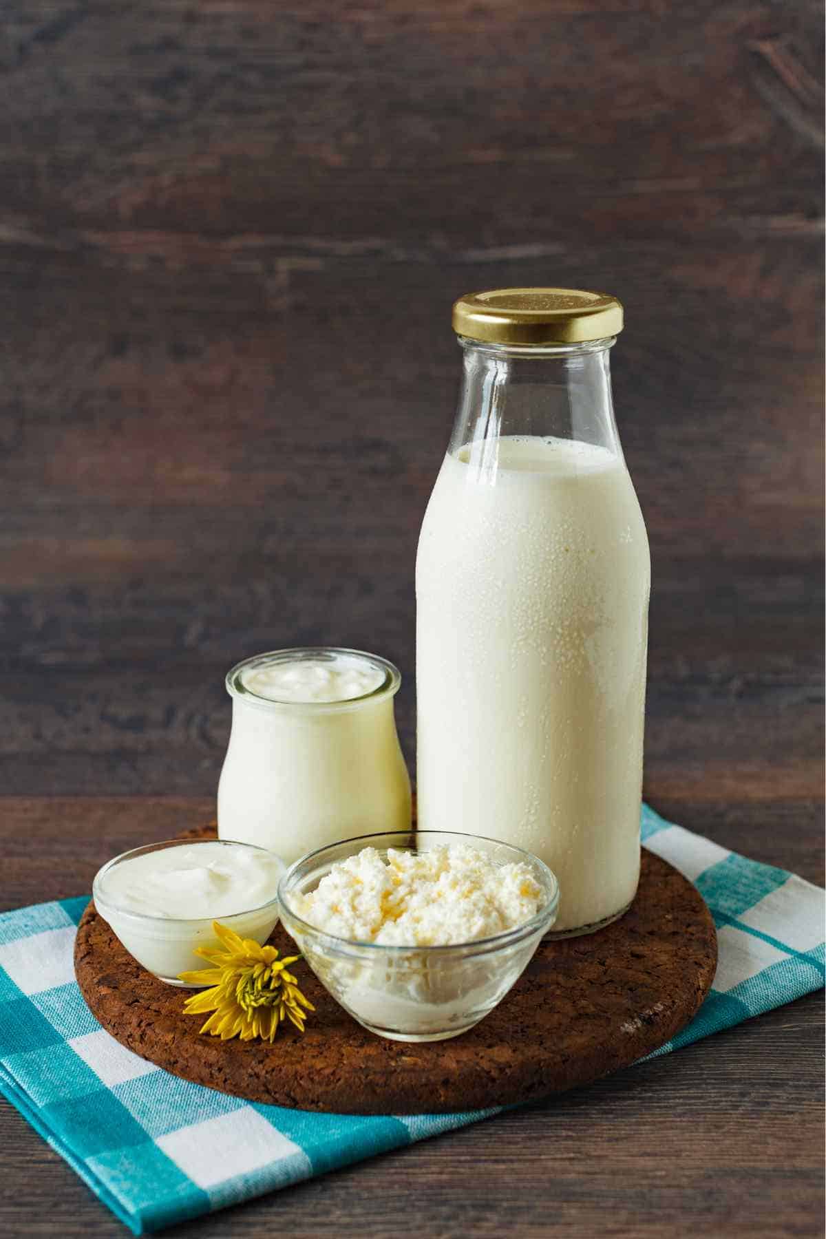 A bottle and a small jar of buttermilk on a wooden surface with a blue and white checkered cloth.