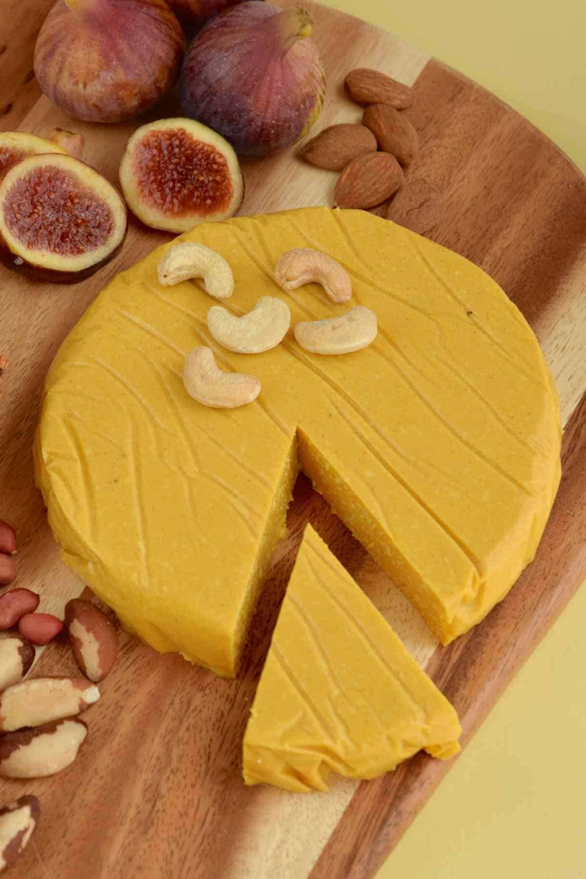 A cashew cheese wheel with a slice cut out on a wooden board.
