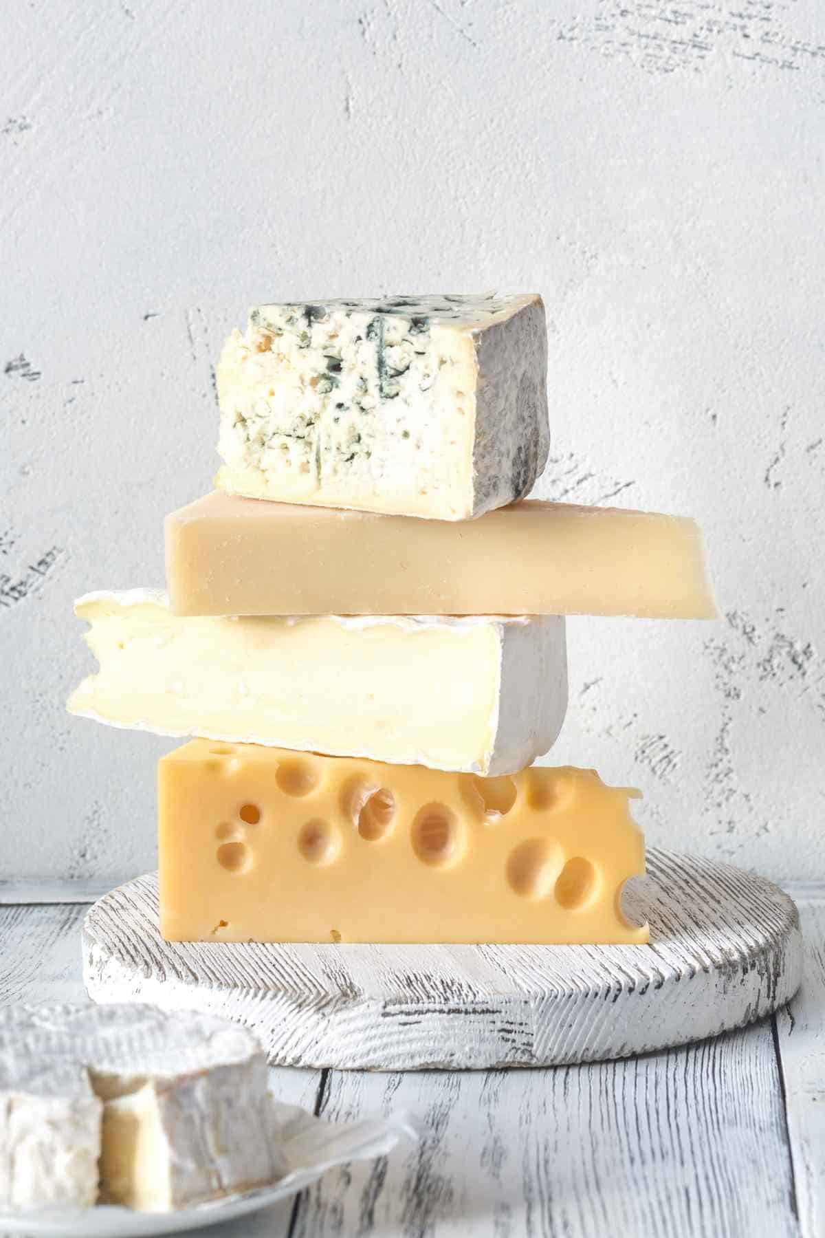 Stack of various cheeses on a white wooden board.