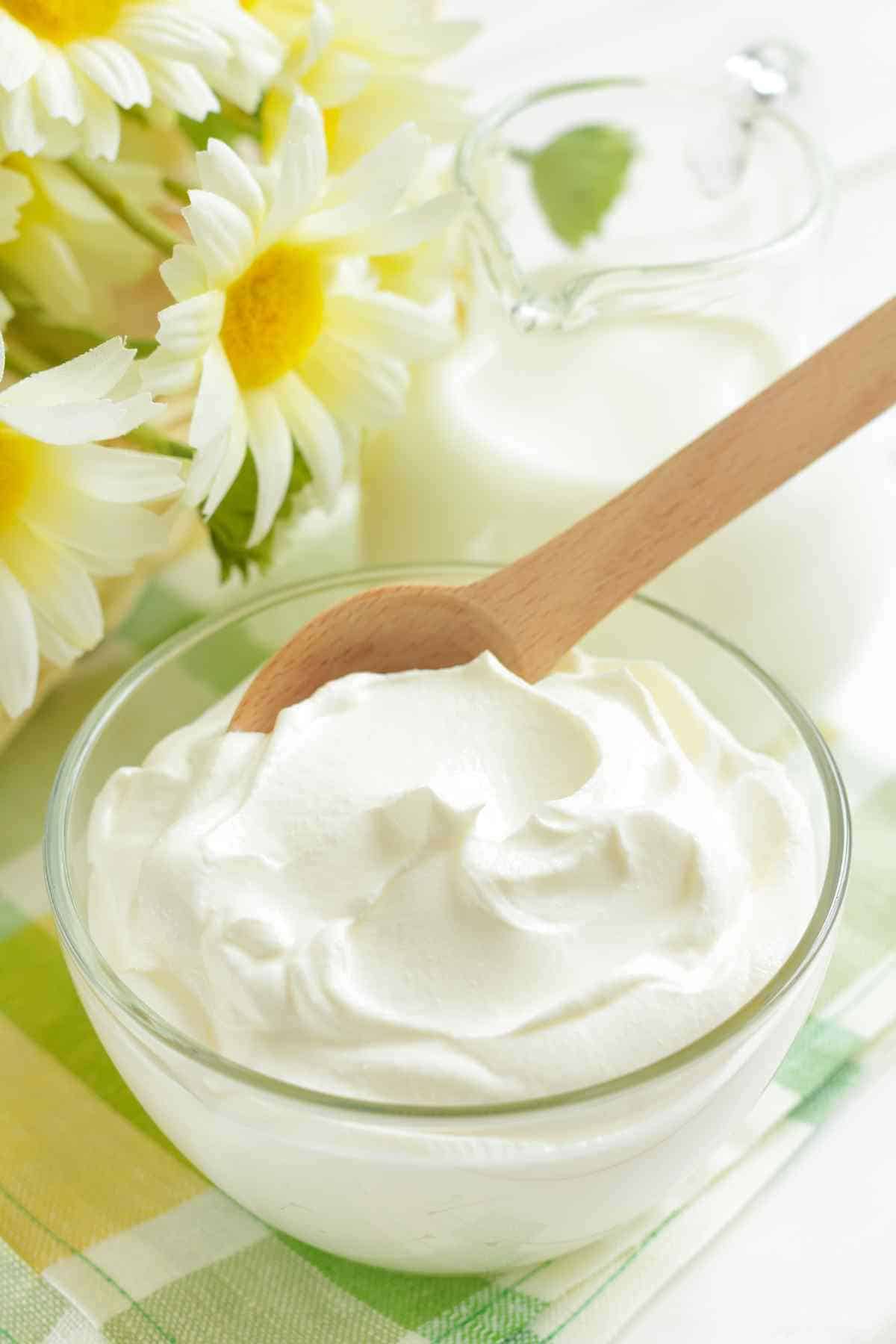 A bowl of cream cheese with a wooden spoon, accompanied by fresh daisies in the background.