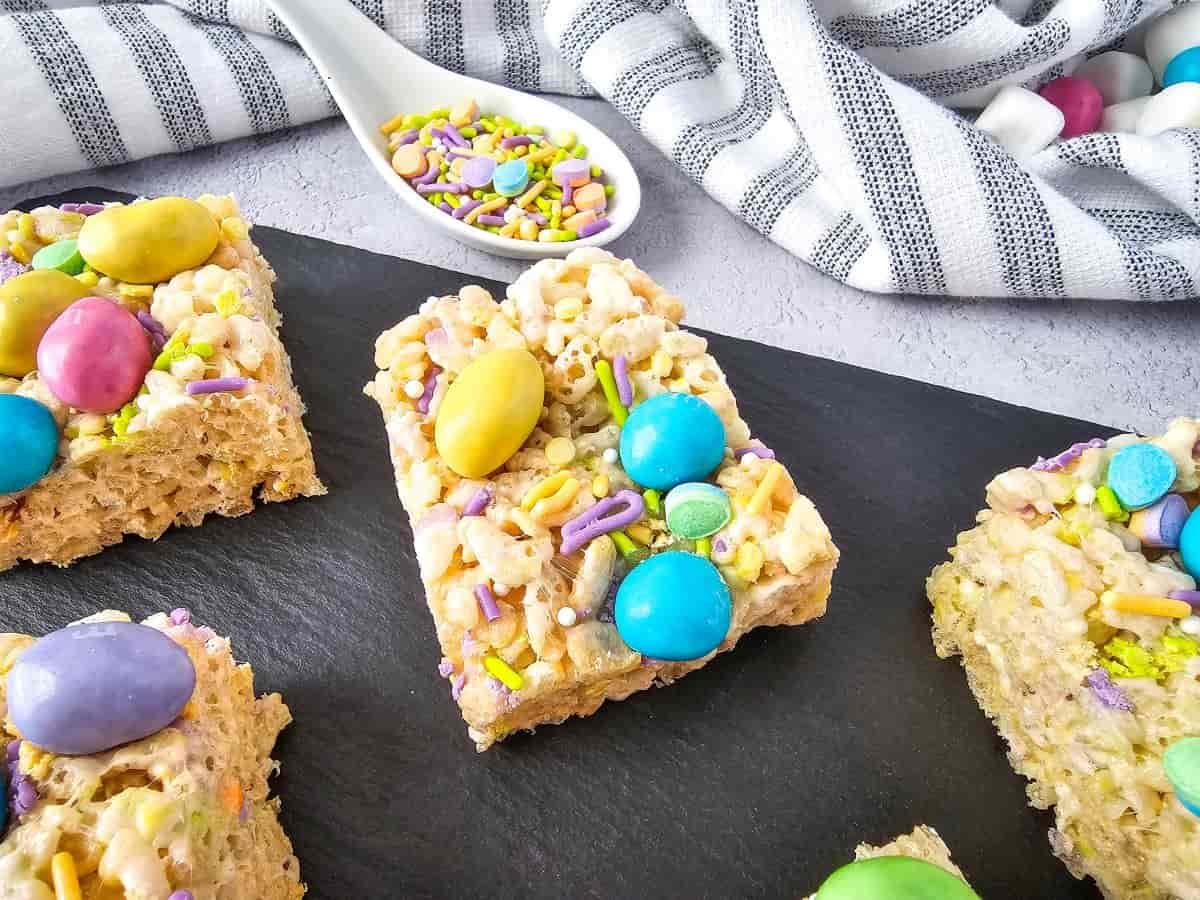 M&M rice krispie treats topped with colorful peanut M&Ms and sprinkles on a serving board.